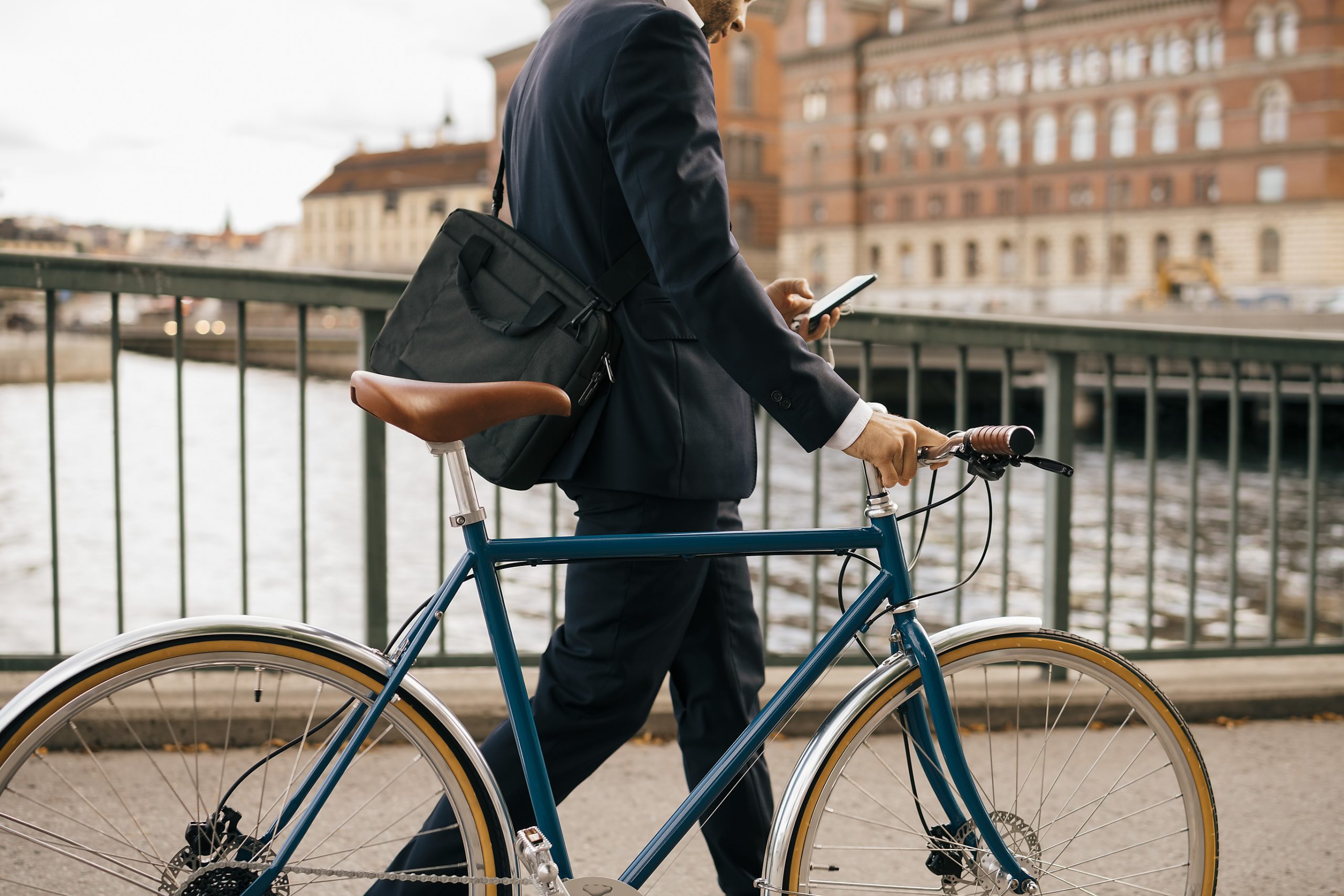 Ausschnitt eines Geschäftsmannes, der mit Smartphone und Fahrrad über eine Brücke läuft