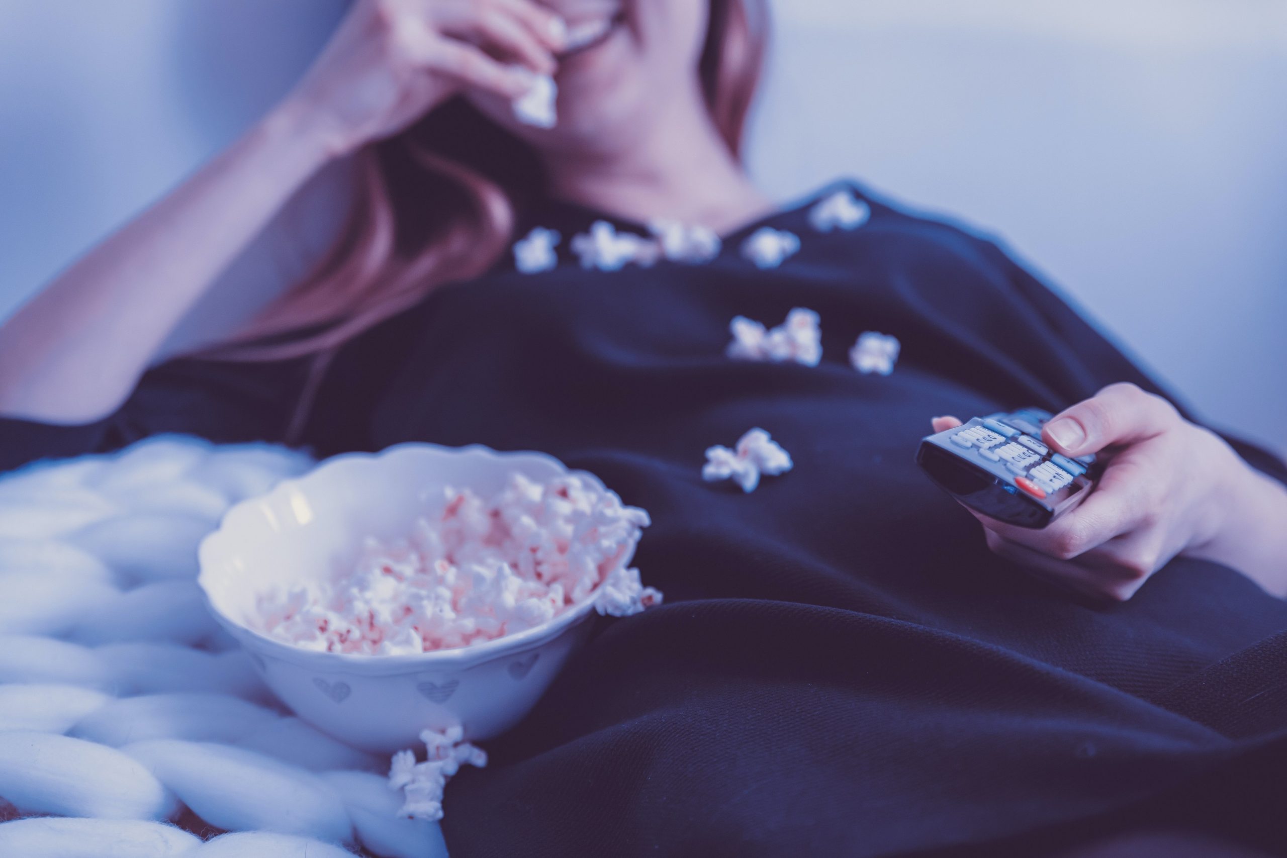 Frau auf der Couch schaut Fernsehen und isst Popcorn