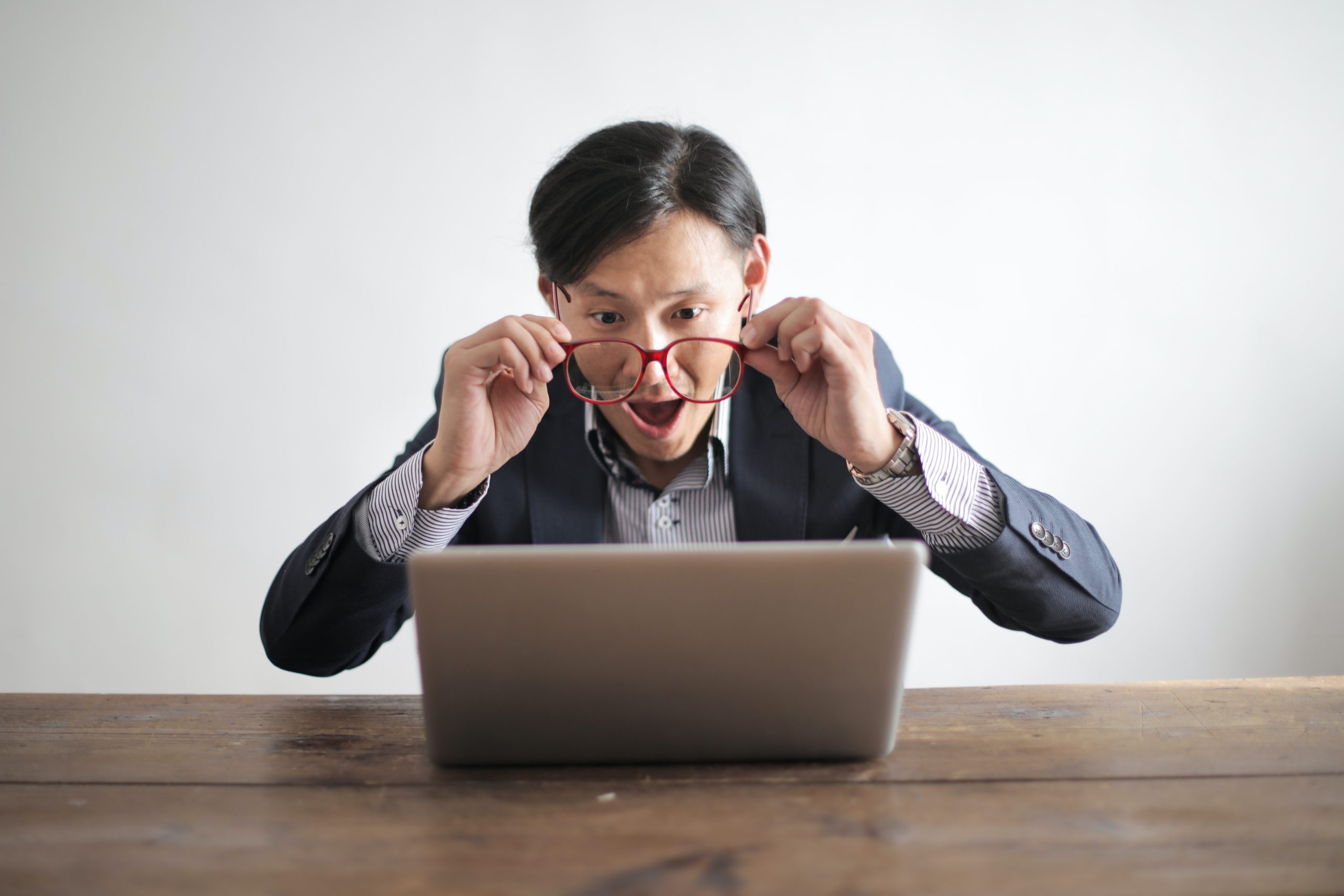 Asiatischer Mann mit roter Brille sitzt vor dem Laptop und zeigt ein überraschtes Gesicht
